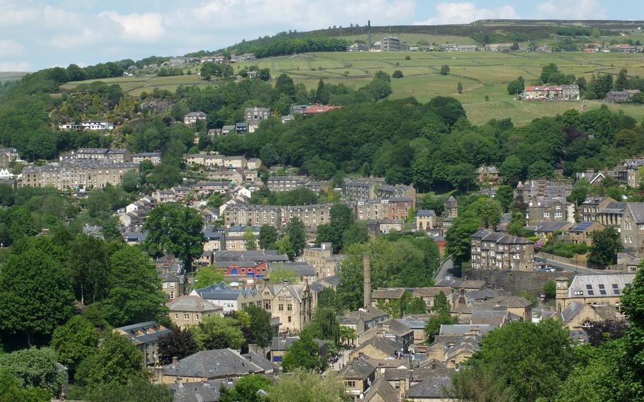 A birdseye view photograph of a town with historical little homes and buildings tan with grey roofs, green trees weave throughout the town. 