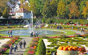 A colorful fall picture with a maze of gardens, a circular fountain, and pumpkins 