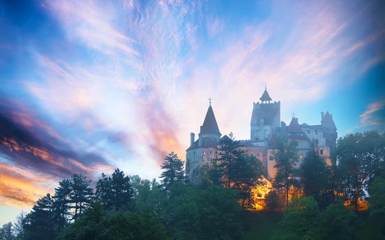 a colorful sunset in the background of Bran Castle hidden in lush green trees