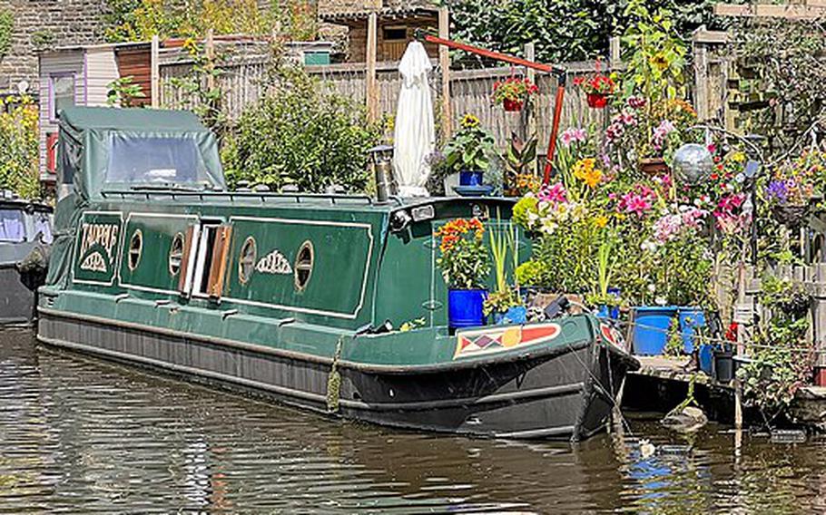 A dark green boat adorned with pink and yellow flowers floats on a brown canal river