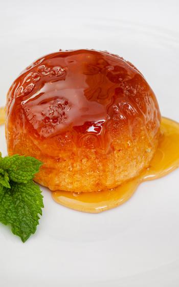 A golden, round cake with a sticky honey-like glaze sitting on a white plate, adorned with green mint sprigs. 