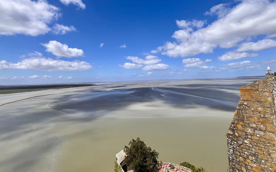 a landscape portrait of sand stretching to the horizon, blue rivers of water come in with the tide. there is a bright blue sky and on the right side, a bit of cobblestone from the fortress. 