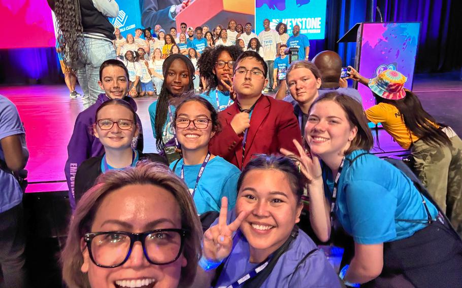 Vogelweh Keystone Club teenagers and their advisor pose while fellow youth participants in the Old Navy modeling show pose for a group shot behind them. 