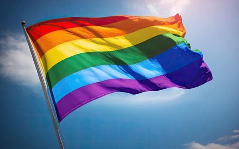 Photo Of Rainbow flag waving in the wind against blue sky with sun rays