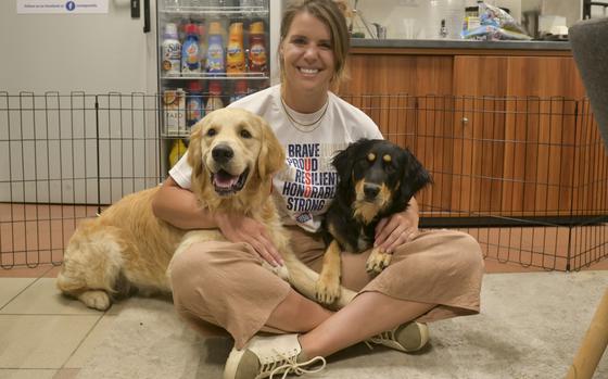 NAVAL AIR STATION SIGONELLA, Italy (July 21, 2023) - Margaret McCullough, USO center manager, poses for a photo with Oliver and Morgan, therapy dogs for Naval Air Station Sigonella’s USO, at the terminal, July 21, 2023. NAS Sigonella’s strategic location enables U.S. allied, and partner nation forces to deploy and respond as required to ensure security and stability in Europe, Africa and Central Command.