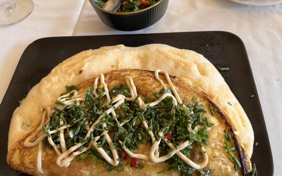 an up-close portrait of a large fluffy omelette garnished with green chives and an orange sauce. 