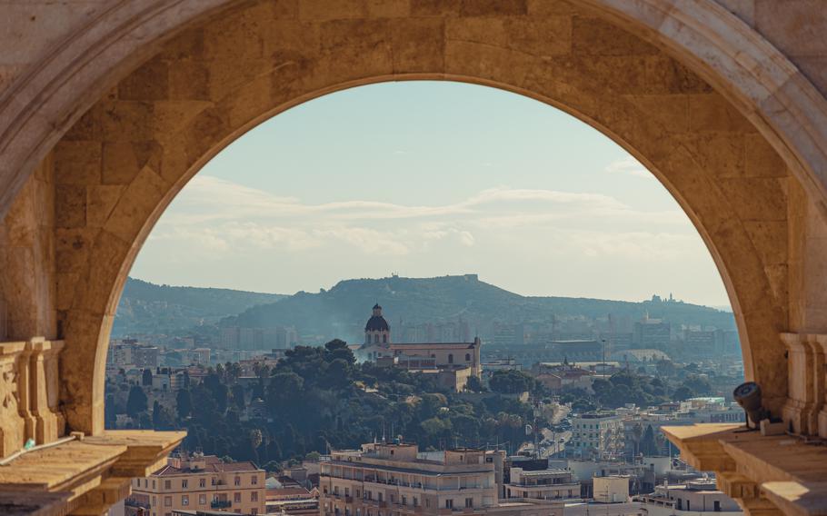 a birds eye view of the old town through an archway. There is a tall hill behind the city and trees woven through the streets.