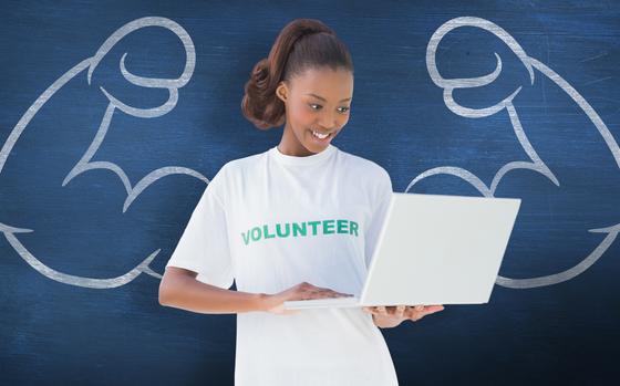 Happy volunteer using laptop  against blue chalkboard