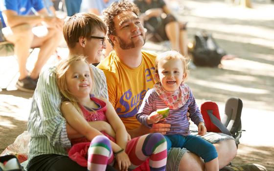 A young family of four sitting down to enjoy the bands at an outdoors music festival.