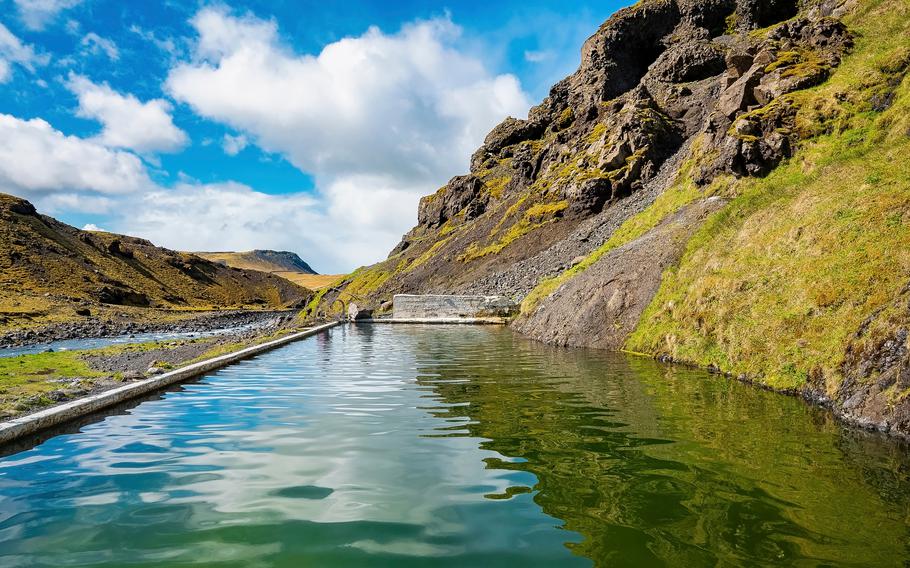 Idyllic view of Seljavallalaug geothermal by mountain. Beautiful natural hot spring pool against sky. Scenic view of oldest swimming pool with reflection in volcanic valley