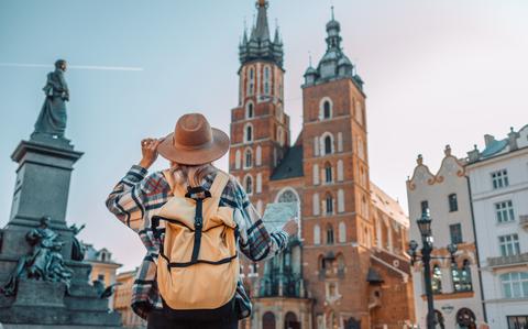 Photo Of Back view of traveler woman walking on old Market Square in Krakow holding tourist map.