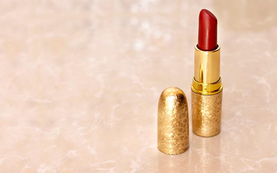 A vintage textured gold tube of red lipstick standing upright with a pink marble background 