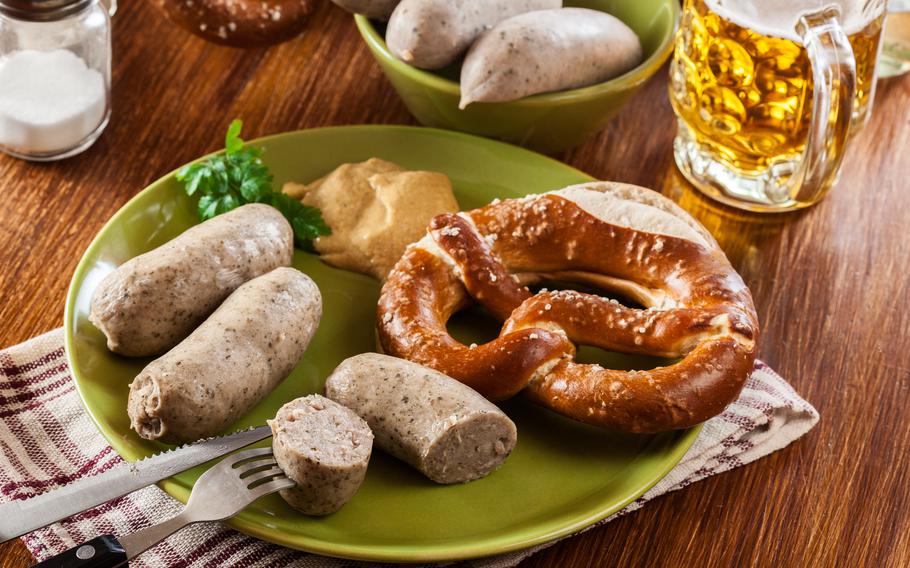 a green plate of two white sausages and a big crispy pretzel with mustard on the side. 