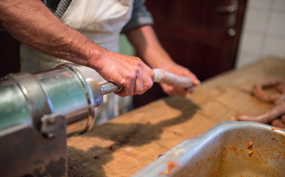 A close-up picture of a man using metal machinery to fill a sausage casing. 