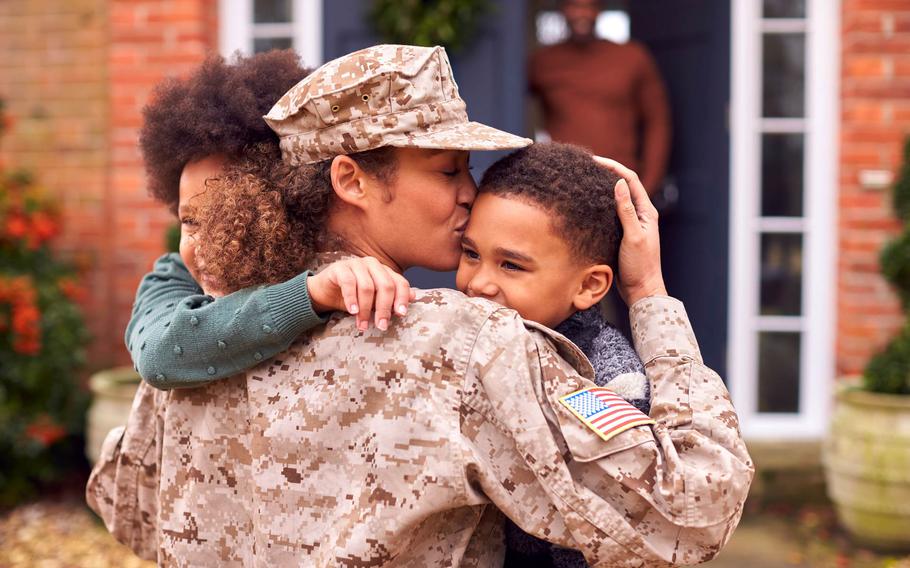 A touching scene of a military service member in uniform reuniting with her children, holding them close with love and warmth. The American flag patch on her sleeve stands out, symbolizing her service and sacrifice. The background shows a cozy home with a wreath on the door, and a family member looking on with a smile, adding to the atmosphere of joy and togetherness.