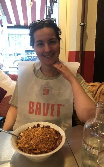 Writer wearing a white bib that reads “bavet” with a bowl of pasta in front of them