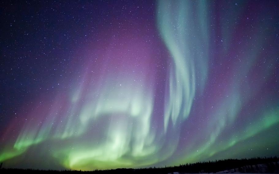 Swirling shades of green and bright purple fill the night sky. 