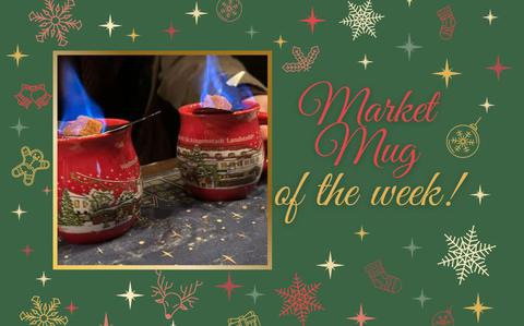 An up-close photo of two red Christmas market mugs with snowy villages painted on the and a flaming sugar cube resting on top of each mug. 