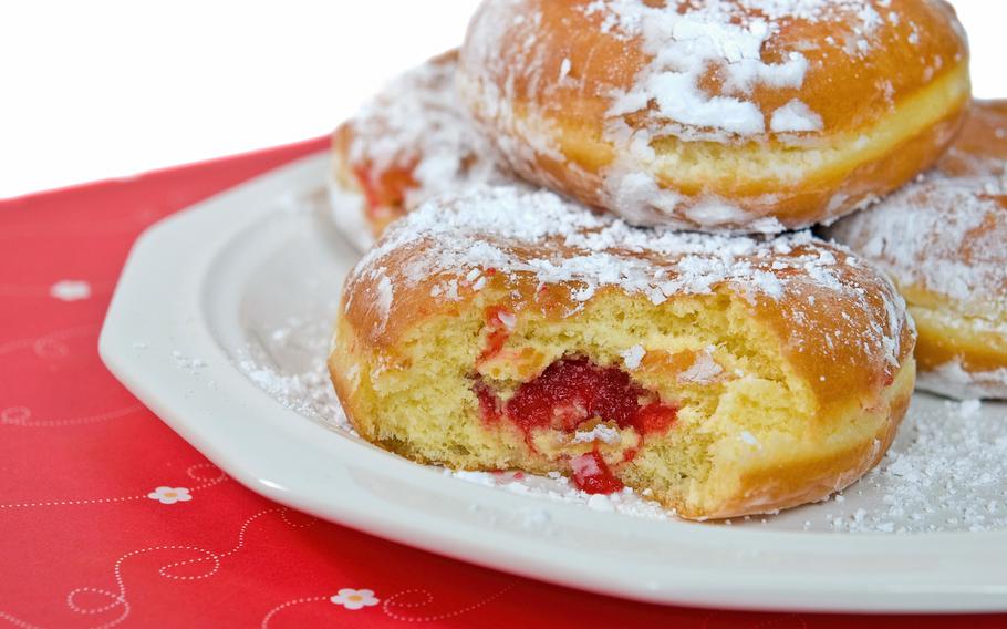 Raspberry paczki on plate. There is a bite taken out of a donut to reveal raspberry jam inside.