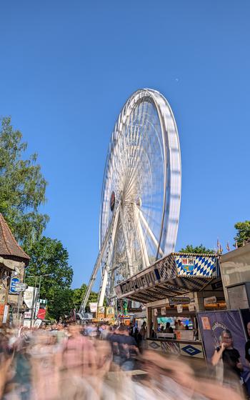 Blurred crowed in a vertical photo with a large white Ferris Wheel in the background
