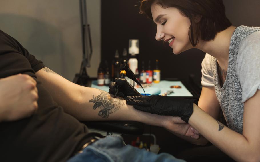 Cheerful woman tattooist doing tattoo with tattoo machine on male arm. 