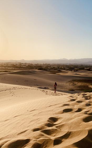 Woman standing in the distance on the sandy dunes.