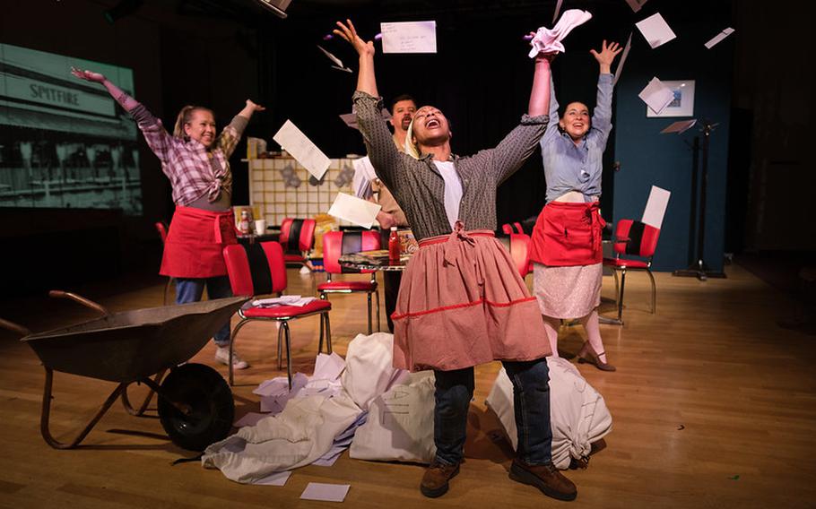 Actors on stage wearing red aprons throwing pages of paper up in the air
