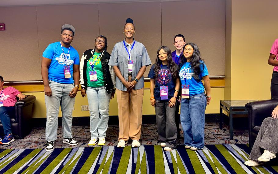 Five teenagers post with Chamique Holdsclaw at a conference center with gold paint and striped green, black and gray carpet.