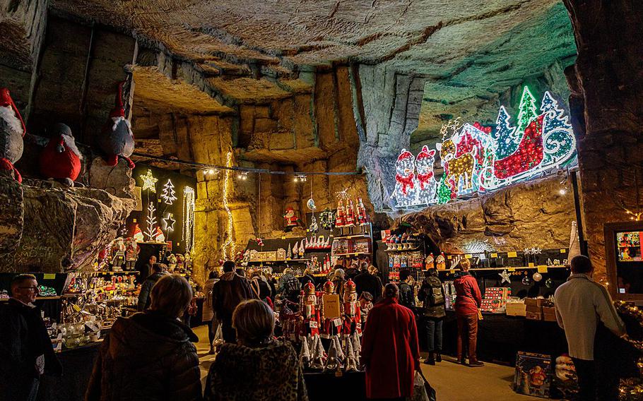 A cozy light brown cave decorated with Christmas lights and Santa, many people are gathered shopping small stalls. 