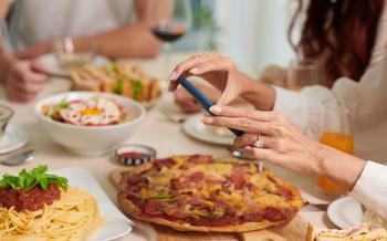 Woman taking picture of a pizza on a wood table.