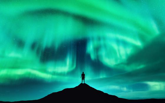 Aurora borealis and silhouette of a man on the mountain peak. Lofoten islands, Norway. Beautiful aurora and man. Alone traveler. Sky with stars and polar lights. Night landscape with northern lights