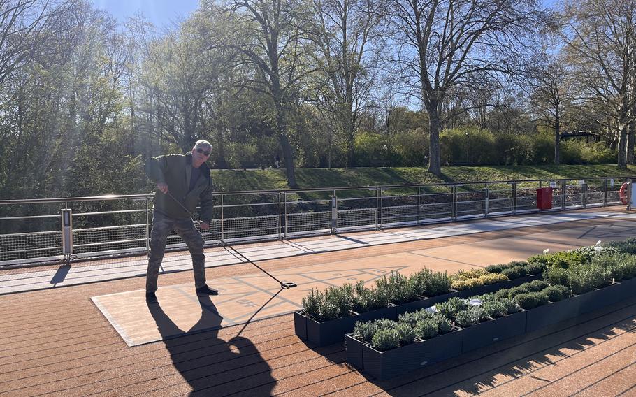 a man plays shuffleboard by a lush herb garden on a cruise ship deck