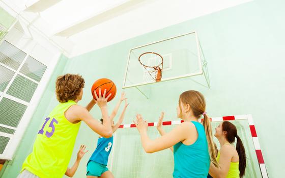 Teenage girls defending against boy throwing ball into the basket during basketball match in gymnasium