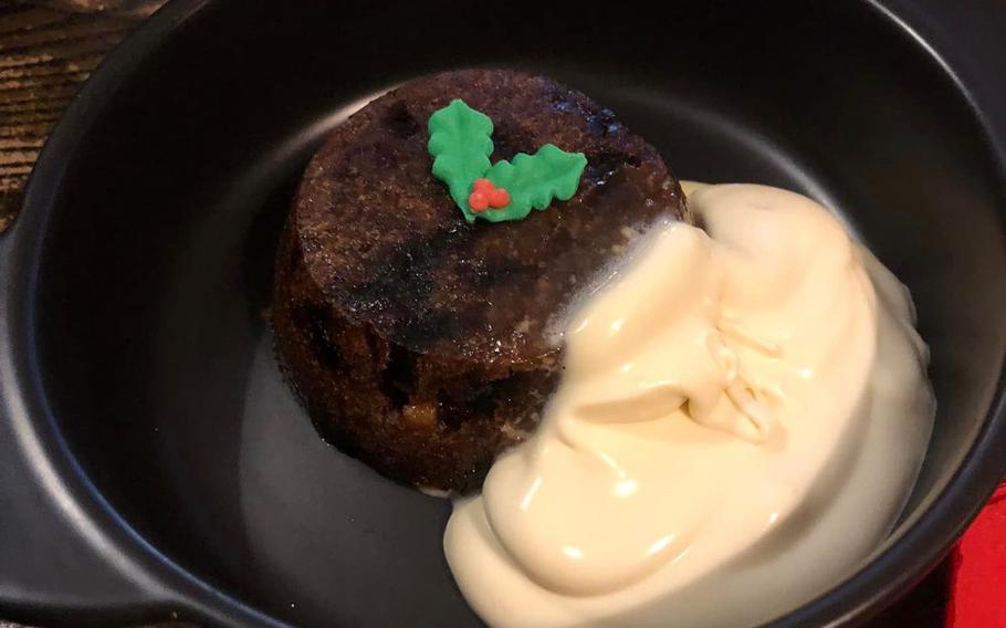 Christmas pudding in black bowl with cream-colored Brandy sauce on the side
