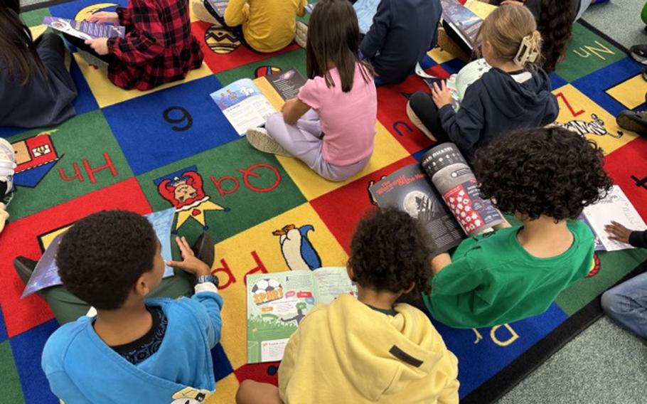 Second-grade class at Ramstein Elementary School library looking at the Fall 2024 “Dandelions” magazine design.