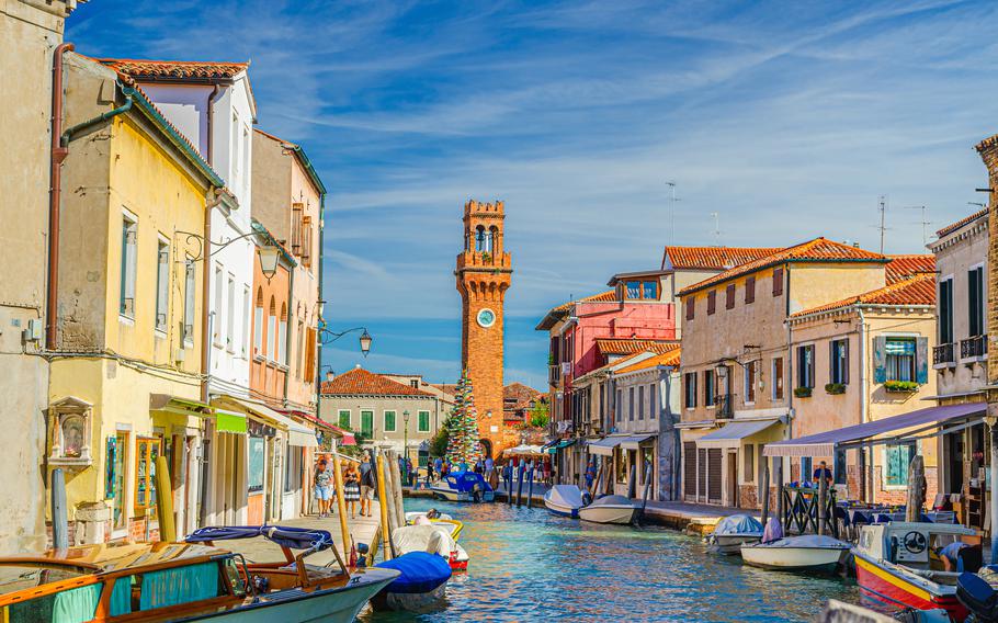 Murano islands with clock tower Torre dell’Orologio, boats and motor boats in water canal, colorful traditional buildings, Venetian Lagoon, Veneto Region, Northern Italy. Murano postcard cityscape.