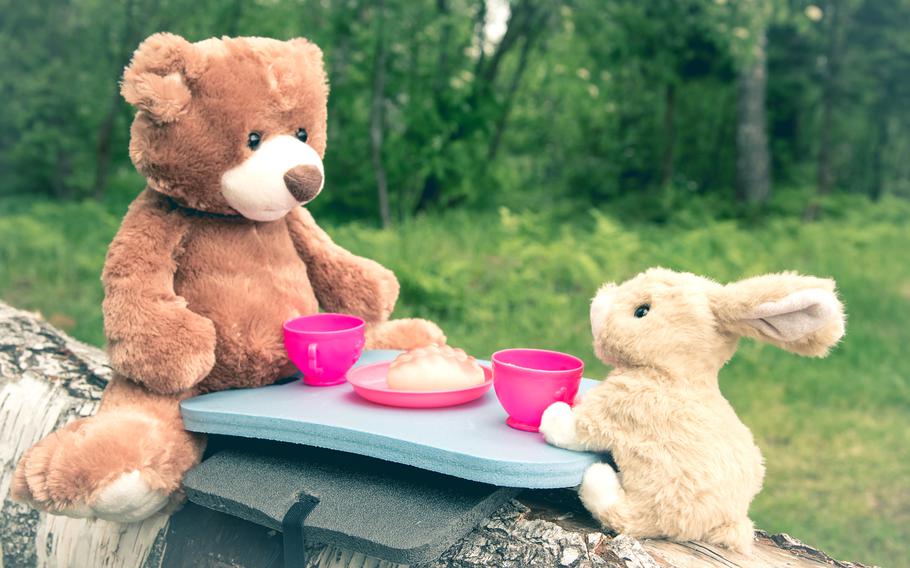 The rabbit and the little teddy bear are sitting on the grass during a picnic in a park.