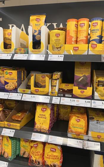 a shelf at a grocery store full of yellow packaged gluten-free breads, cookies, cereals and more