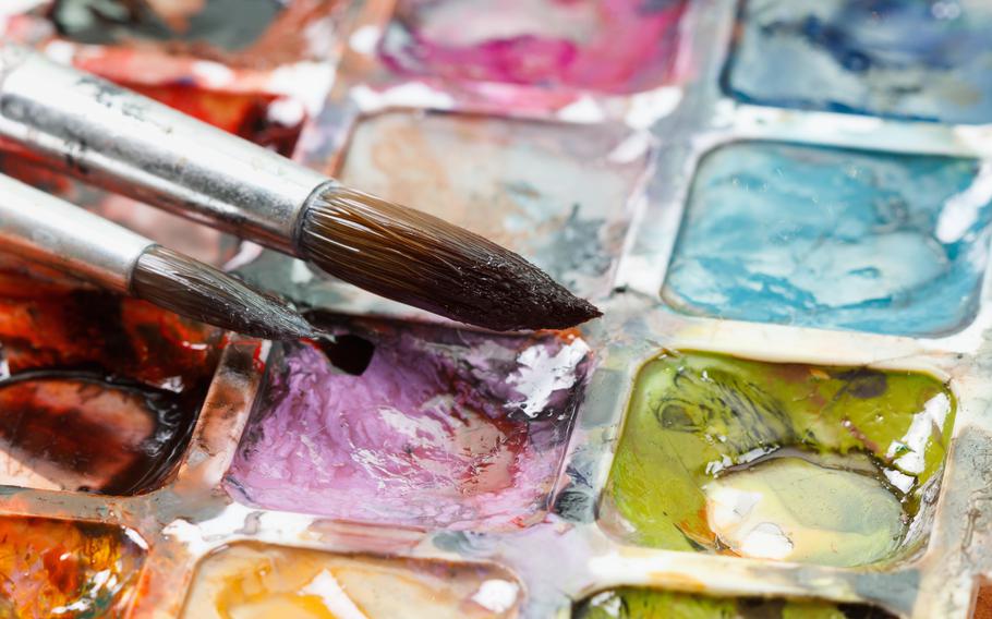 Two paint brushes dip into wet, water color paints. 