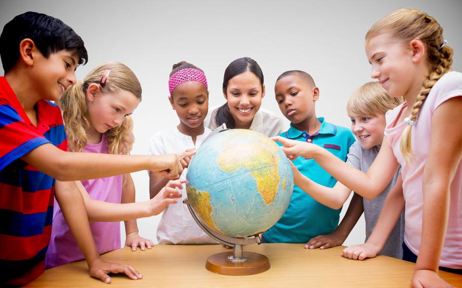 Cute pupils and teacher looking at globe in library  against grey vignette