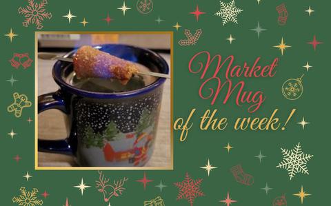 Photo Of An up-close picture of a blue mug with snow and evergreens, a rolled-doughy treat balances on top and emits flames