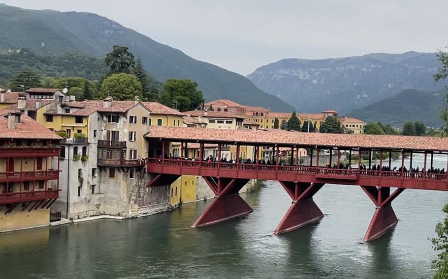 Bassano del Grappa on a cloudy day. A red bridge sits atop a body of water with mountains in the background