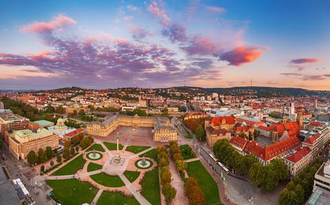 Photo Of An aerial view during a purple sunset of stuttgart with a green, manicured lawn, the place, and red-roofed buildings