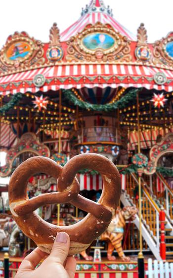 The girl is holding a traditional German pretzel. Carousel and celebration in the background.
