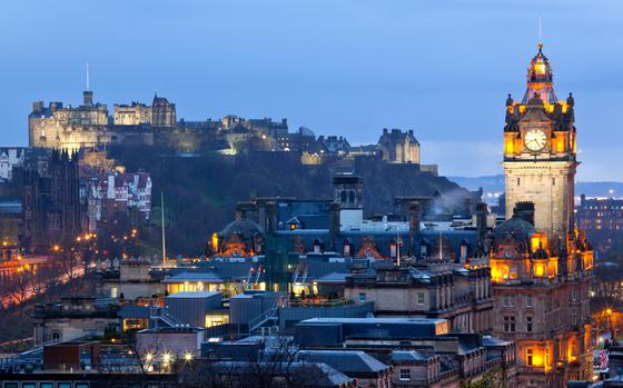 Point of view from Calton Hill, Scotland at dusk: On the right, illuminated clock tower and buldings; to the left and back of the the picture, illumniated Edinburgh Castle