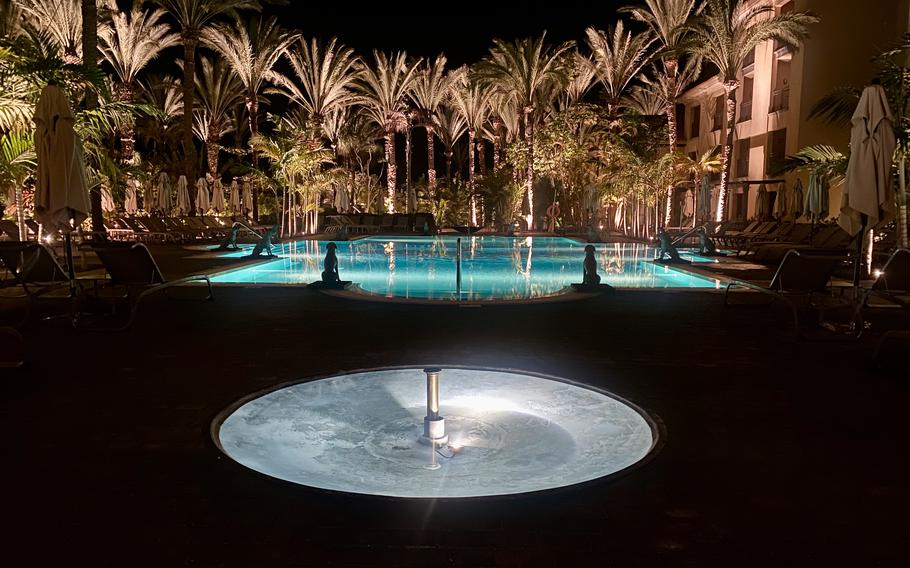 Resort pool and palm trees at night lit up with lights from the bottom of the pool