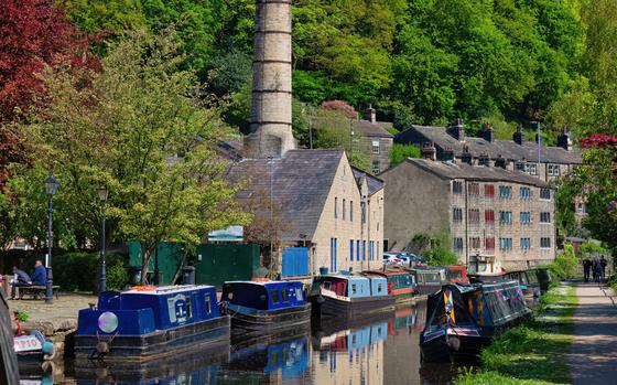 Photo Of A historical town, buildings with blue, red and purple windows. Blue and red boats floating in front of the building on a reflective canal. 