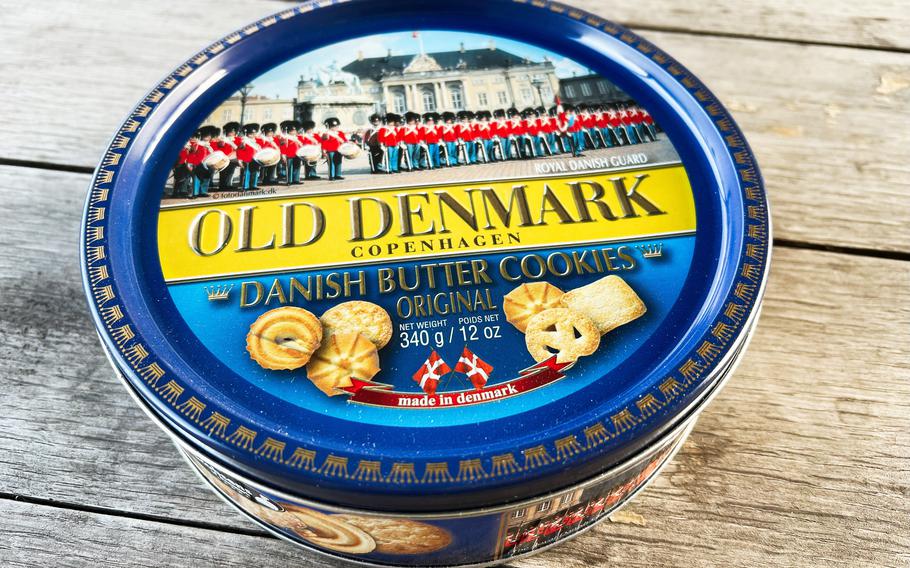  A metal tin containing original Danish butter cookies, displayed on a rustic wooden surface. The tin features a Copenhagen cultural theme with festive branding, showcasing premium confectionery. 
