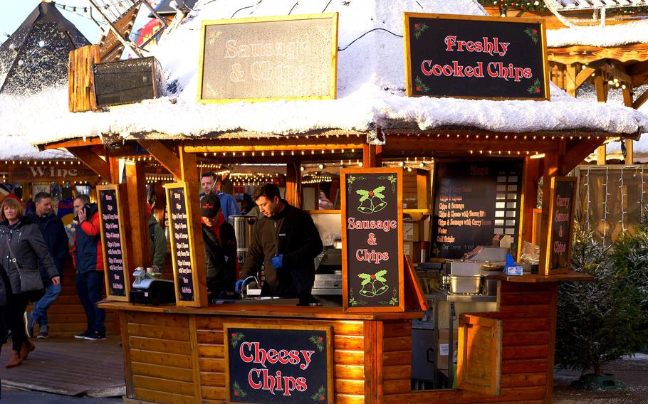 A snow covered, wooden hut selling cheesy chips and sausage and chips. 