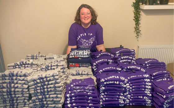 Meghan Mitchener behind a stacks of purple and grey shirts she created